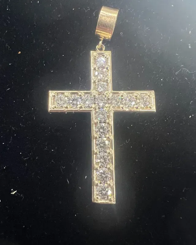 A gold cross with diamonds on it is on a black surface