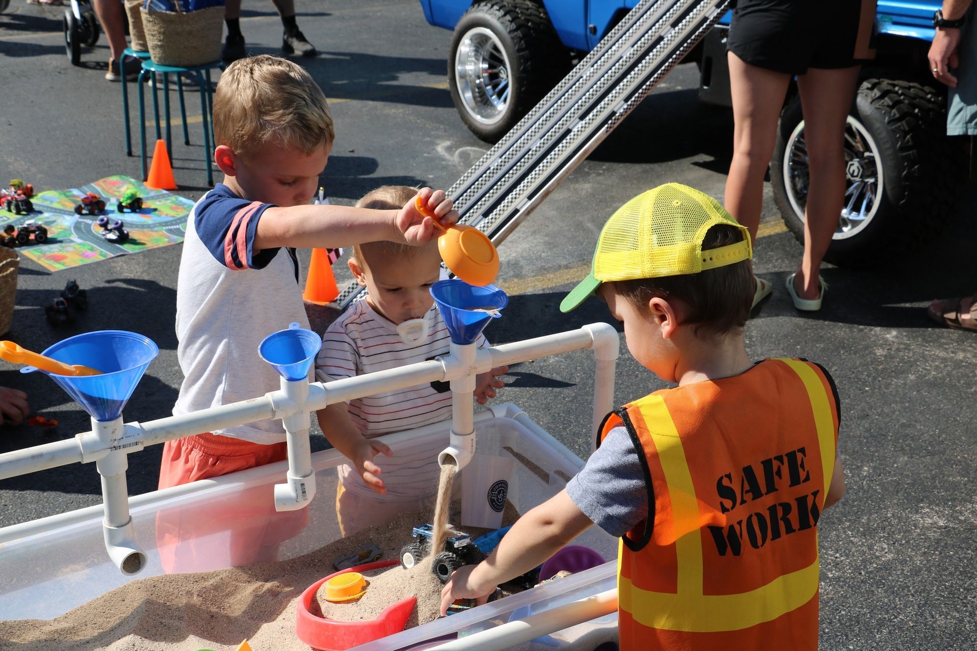 Two young boys are playing in a sandbox with a safe work vest on.