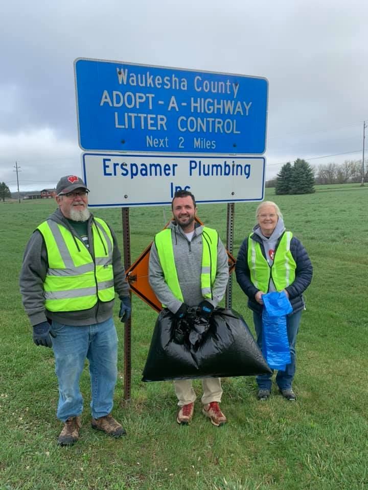 Three people are standing in front of a sign that says adopt a highway litter control.