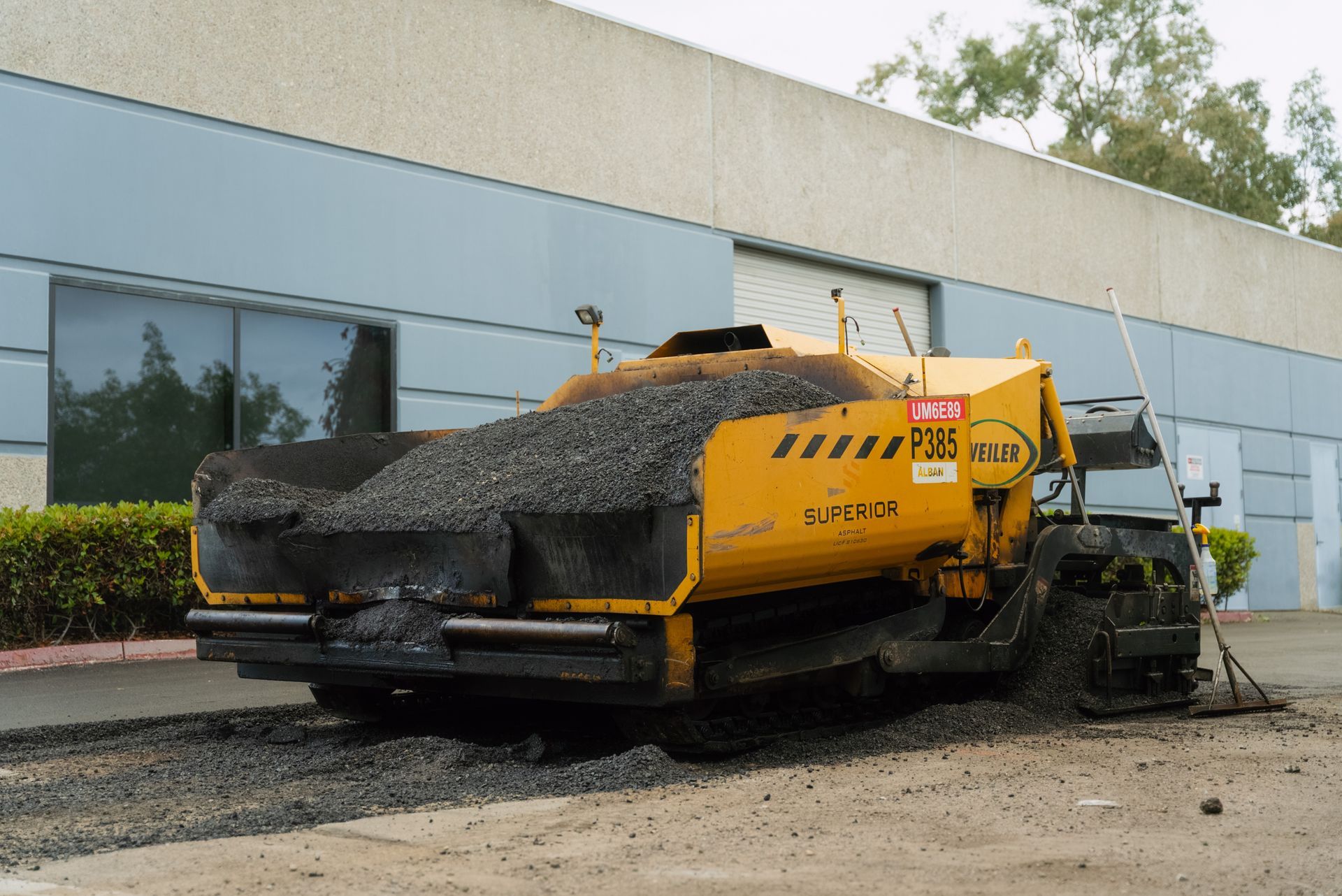 Yellow road paver covered in asphalt on a construction site beside a building