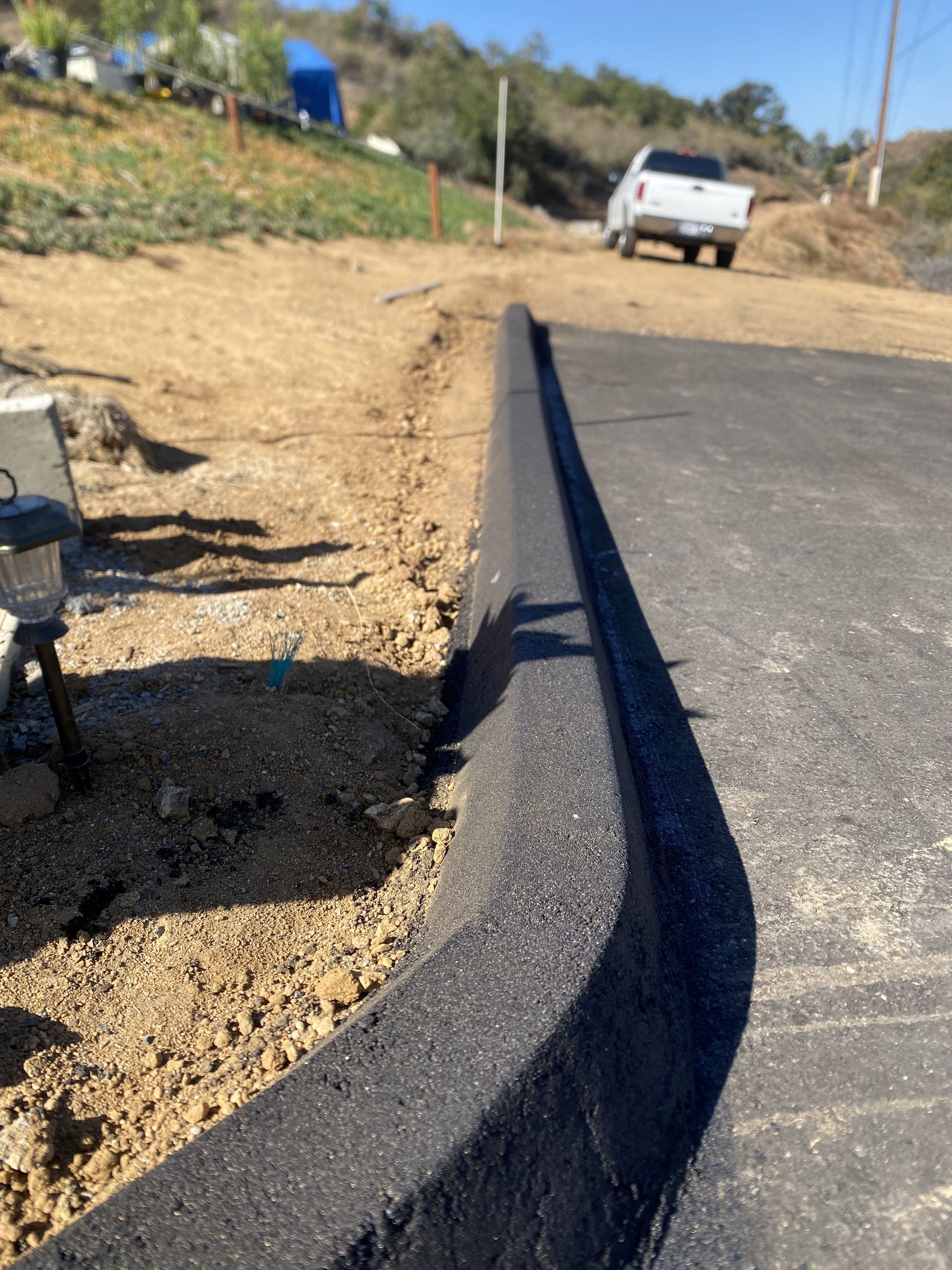 Fresh black curb along a newly paved road beside a gravel shoulder and parked white truck
