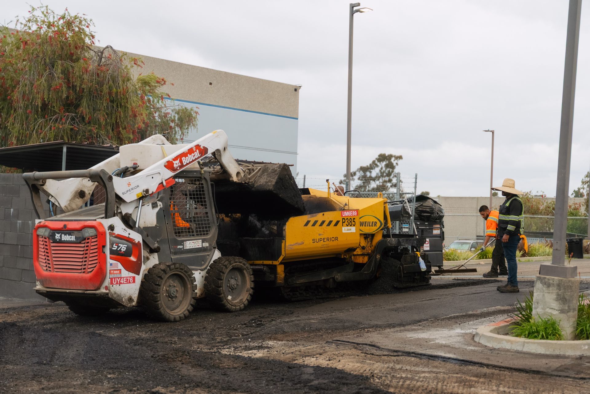 Roadwork crew operating a skid steer and asphalt paver on a street corner
