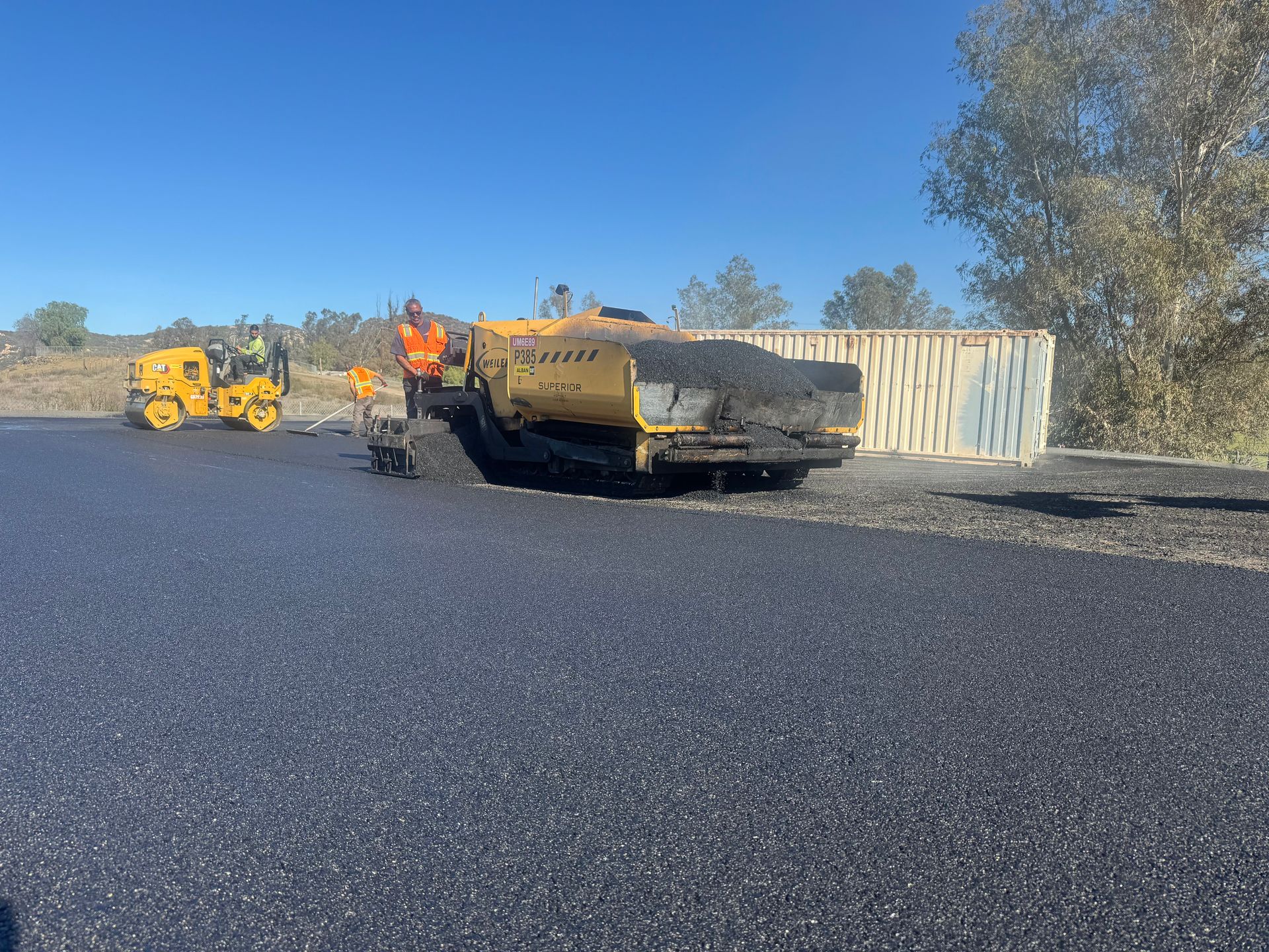 Yellow road construction pavers on fresh black asphalt under a clear blue sky