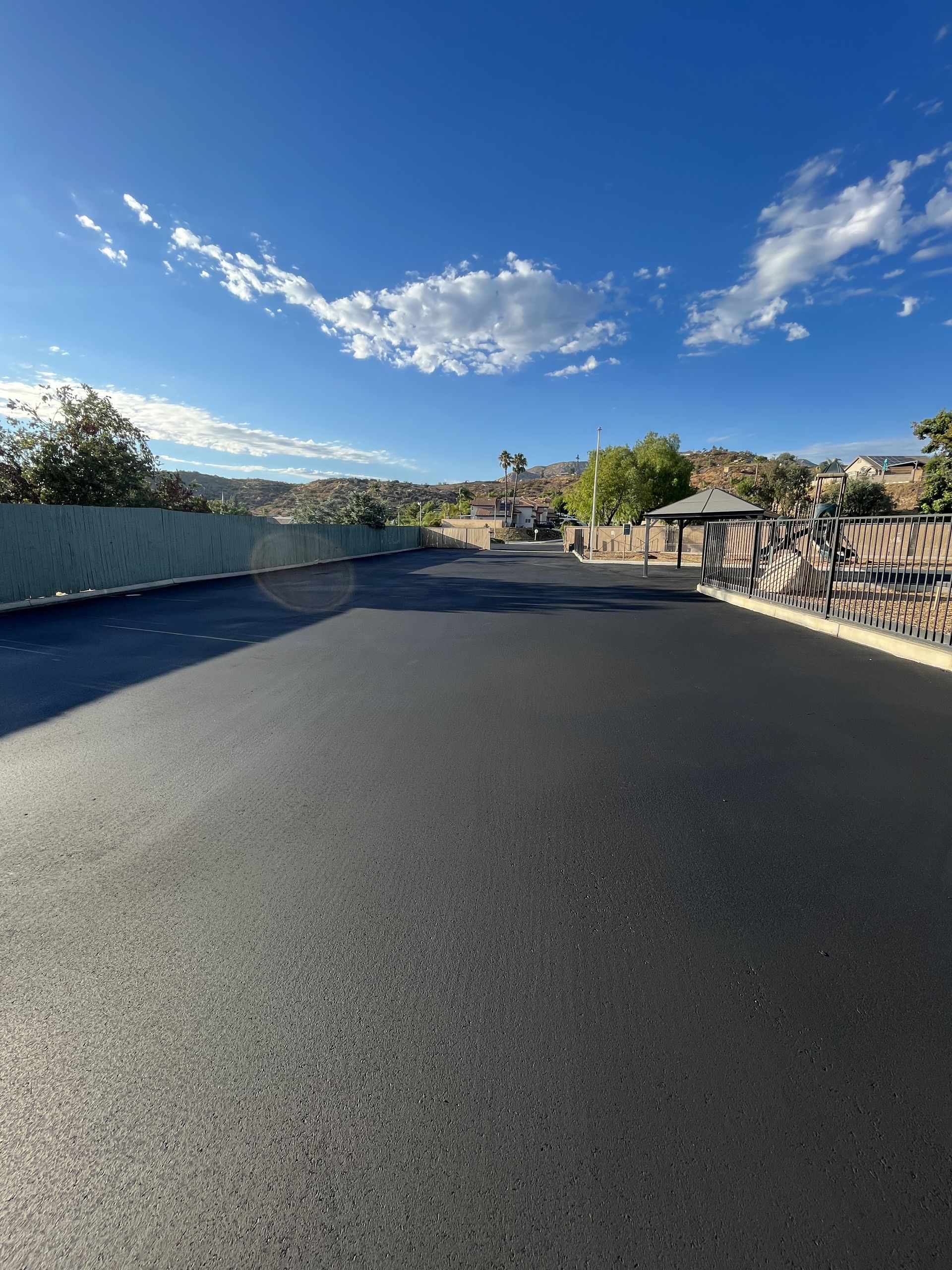 Wide paved road beside stone walls and houses under a bright blue sky with scattered clouds.