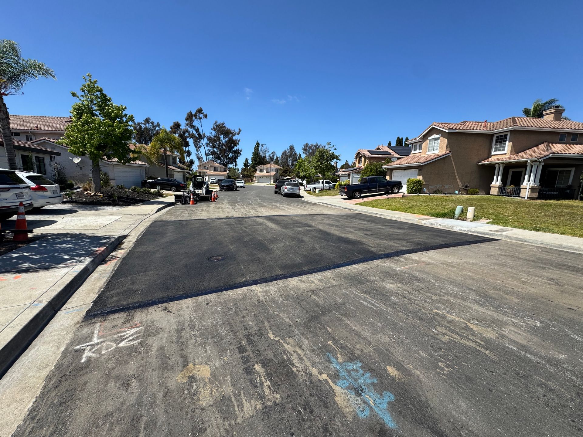 Residential street under construction with fresh asphalt, sidewalks, and houses on both sides under a clear blue sky