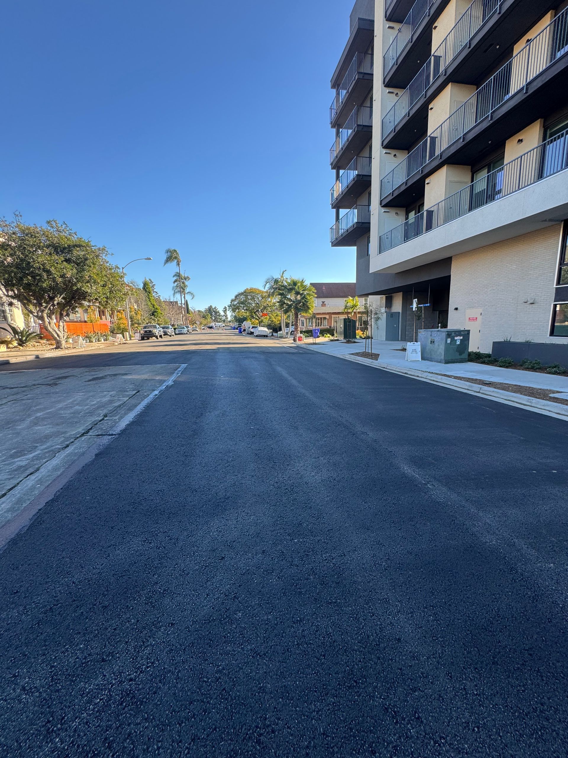 Empty paved road beside a modern apartment building under a clear blue sky