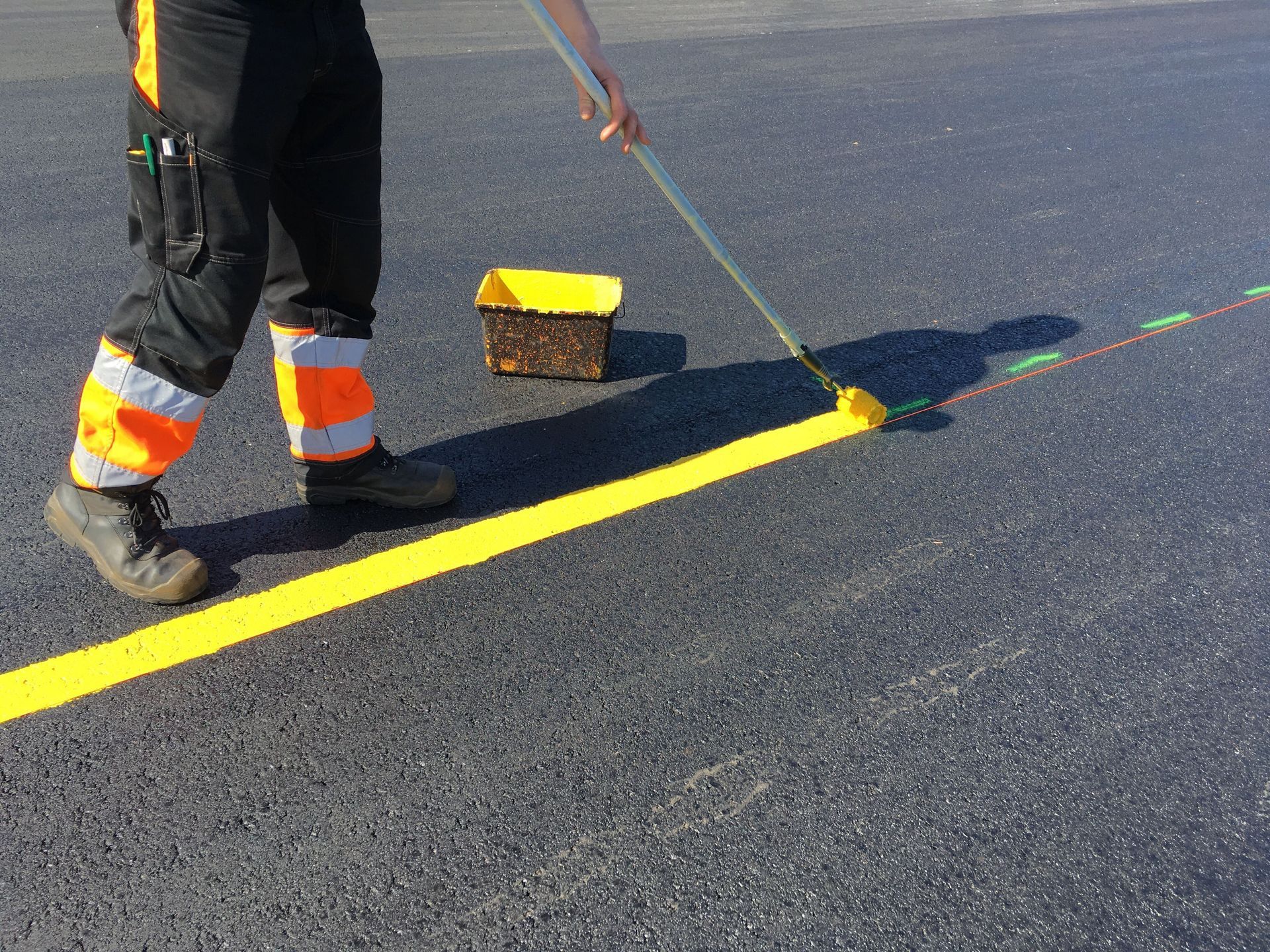 Worker painting a bright yellow line on asphalt with a roller