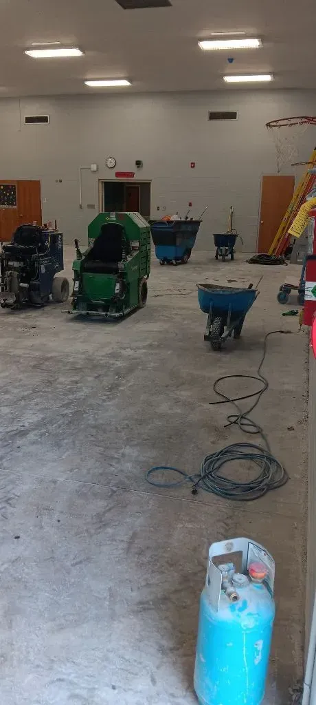A workshop interior with equipment on a concrete floor, including a green machine, and a blue propane tank in the foreground.