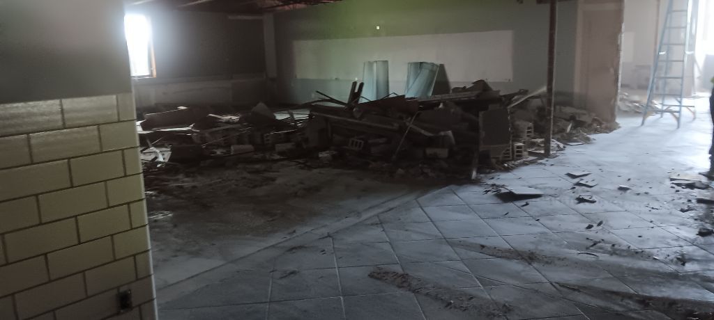 Interior view of a demolished room with piles of rubble. A window at the back emits light.