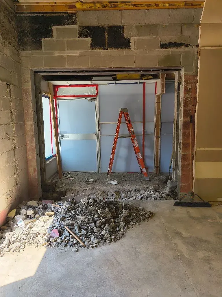 A doorway being renovated; debris on floor, orange ladder inside, exposed concrete block and brick.