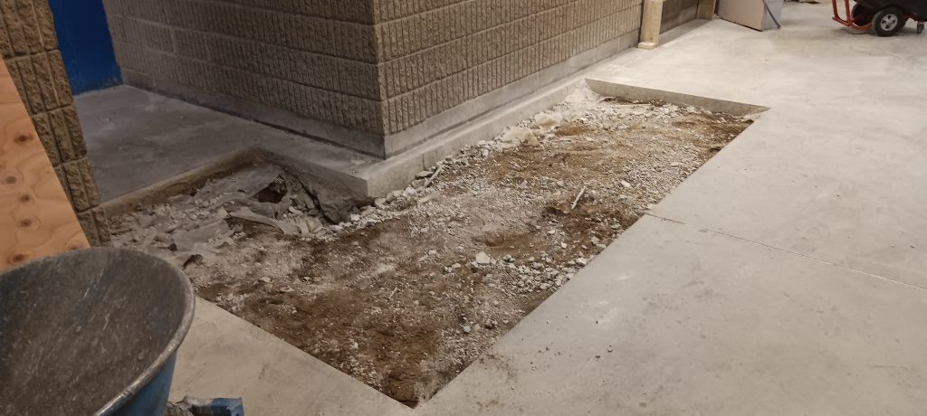 Construction site with a hole in the concrete floor next to a brick wall. Debris fills the hole.