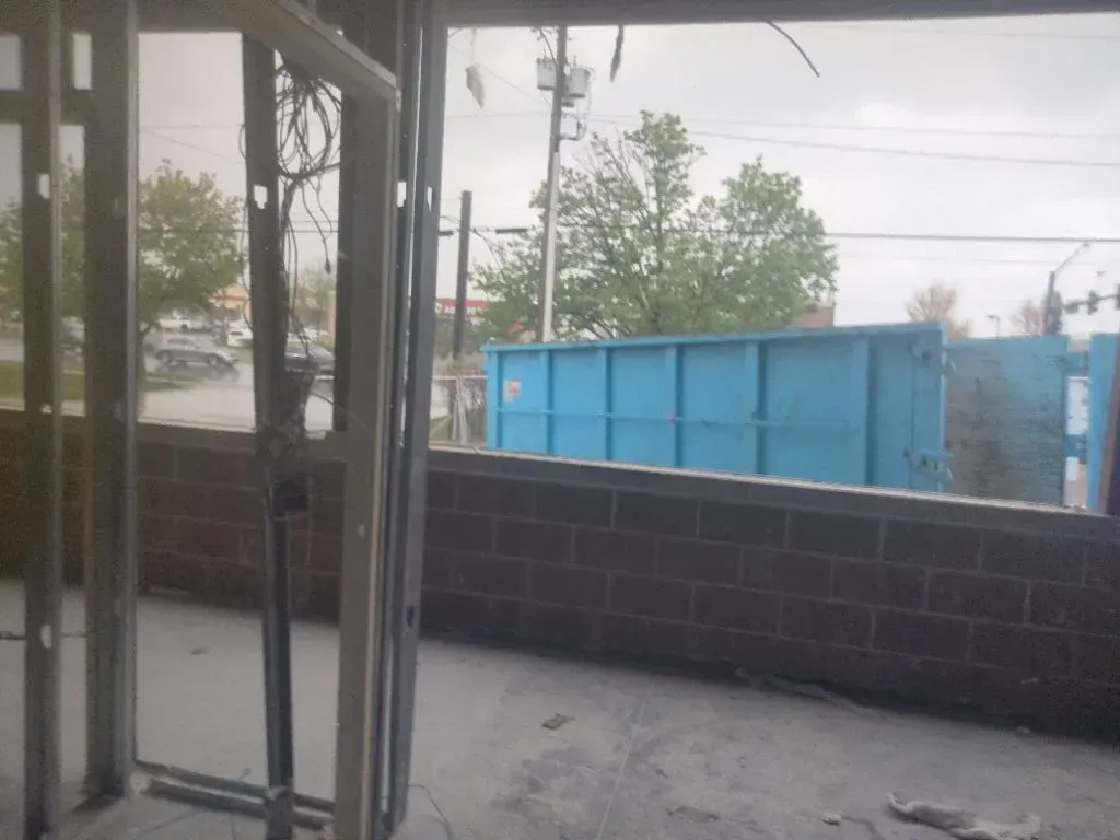 Interior view of construction site, steel framing, brick wall, blue dumpster in the distance.
