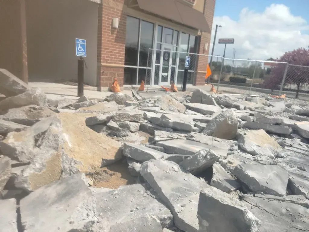 Sidewalk destroyed in front of a building with a handicap parking sign; construction cones present.