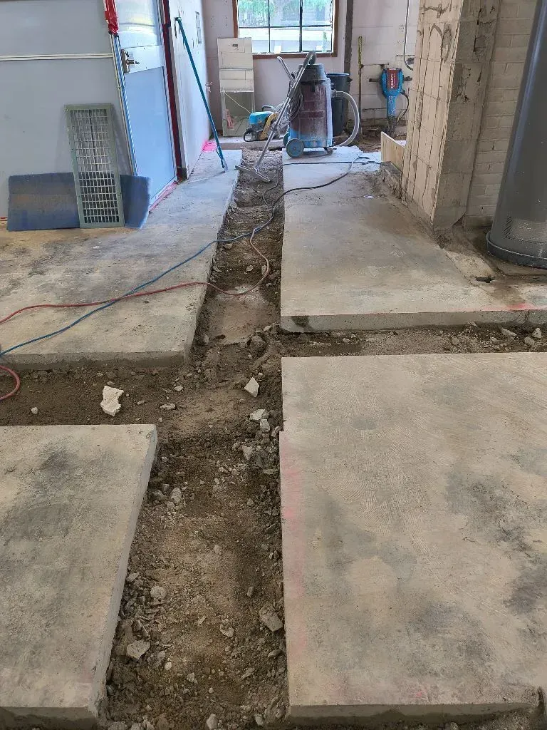 Concrete floor with trench dug through it, demolition in progress inside building.