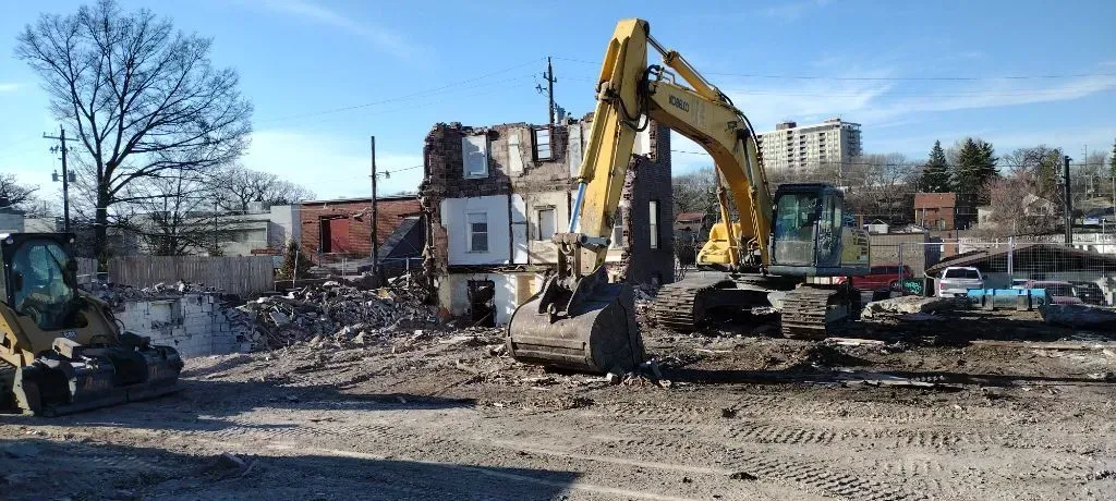 Yellow excavator and bulldozer demolishing a building under a blue sky.