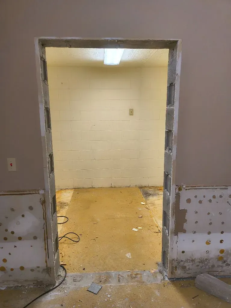 A doorway with exposed framing, revealing a small room with a concrete floor.