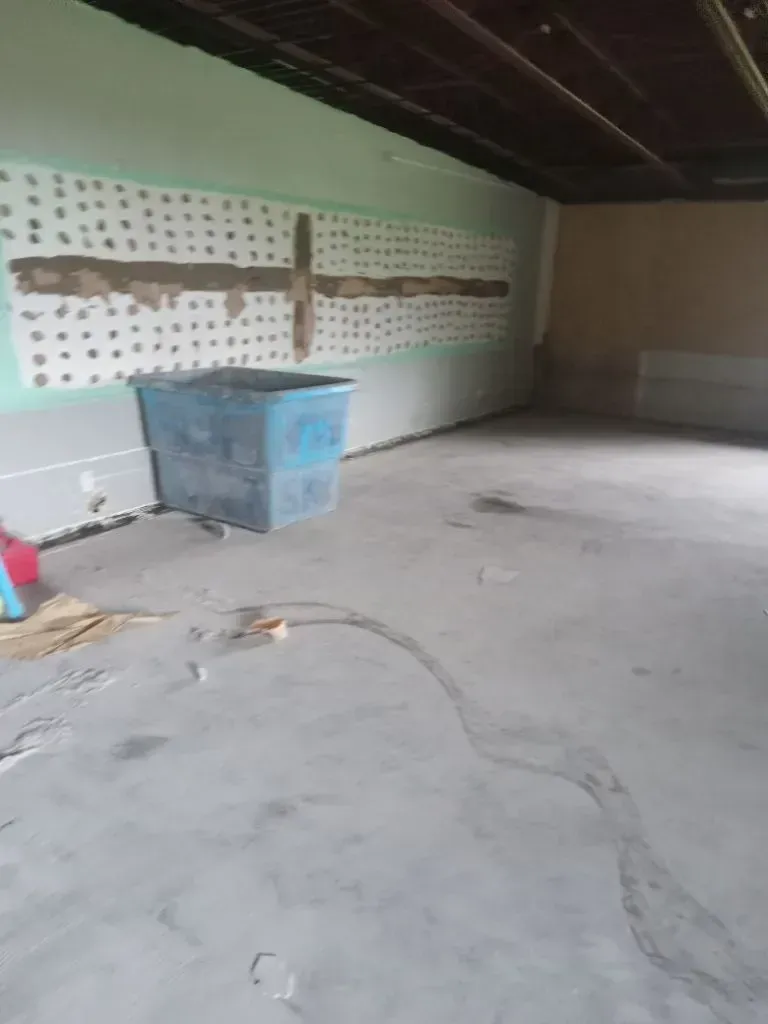 Bare basement with exposed beams and wall with drywall, blue bin on floor.