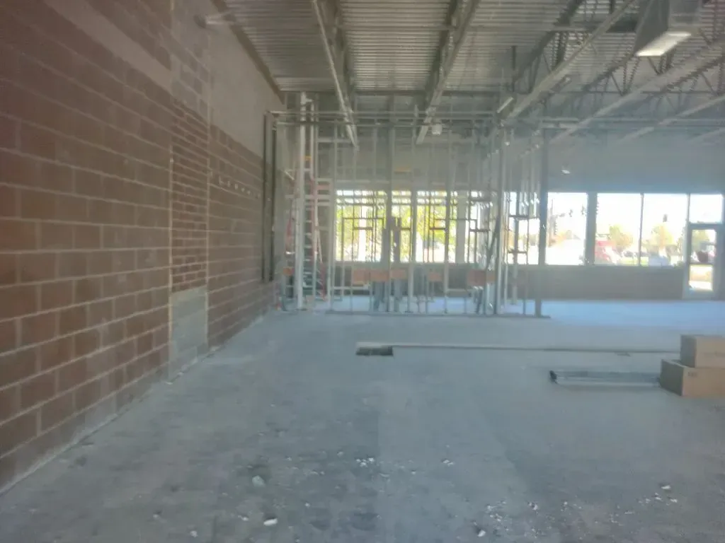 Interior of a commercial space under construction with brick walls, metal framing, and concrete floors.