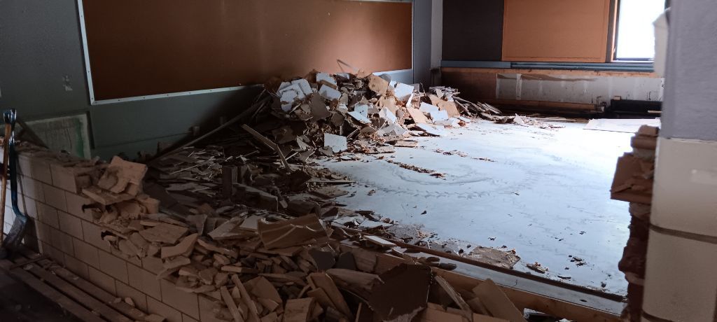 Room interior with debris from a wall demolition. Brown and white tiles, concrete floor, and brown wall.