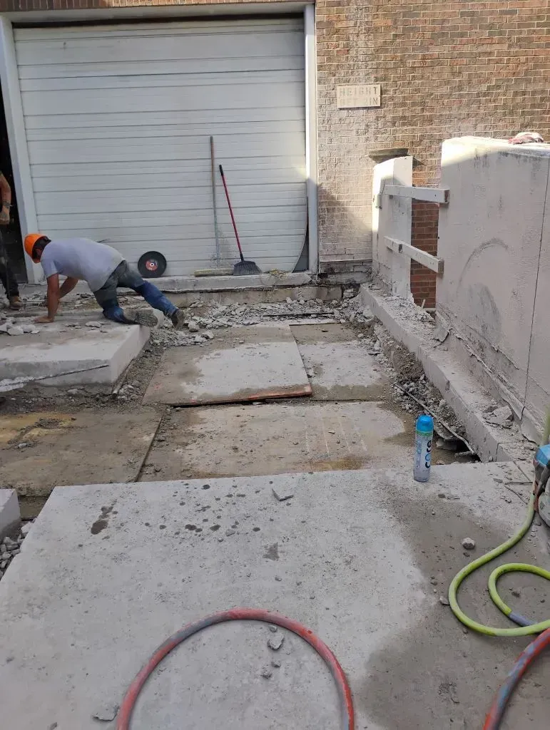 Workers demolishing concrete slabs near a garage door.