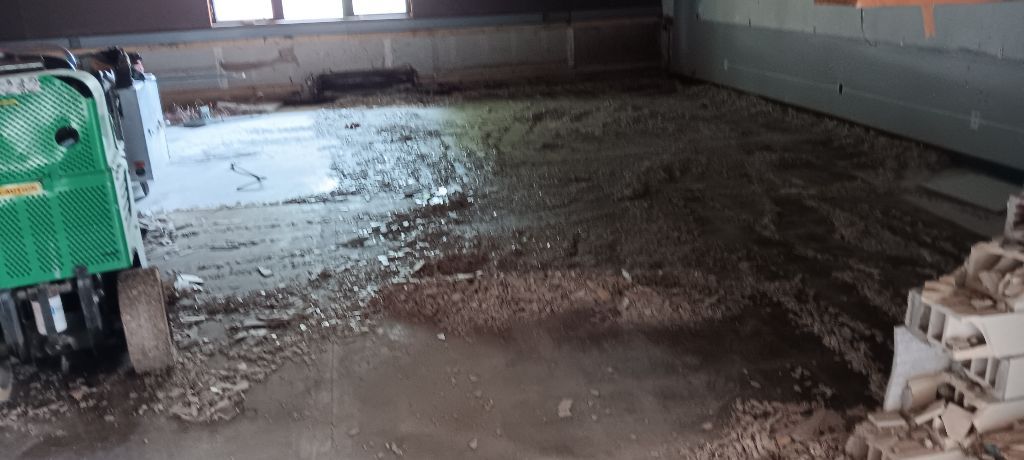 A demolition site with a green machine removing the floor. Brick and debris scattered around.