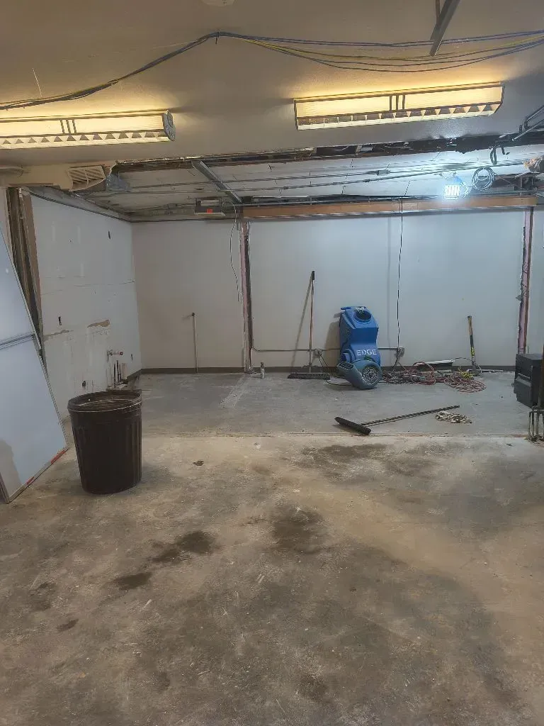 A room under construction with exposed walls and ceiling. A trash can and construction equipment are present.