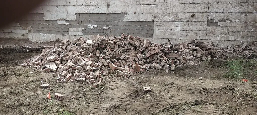 Pile of brick rubble in front of a deteriorating brick wall on a muddy ground.
