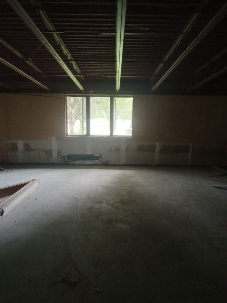 Empty, unfinished room with three windows, concrete floor, exposed ceiling beams.