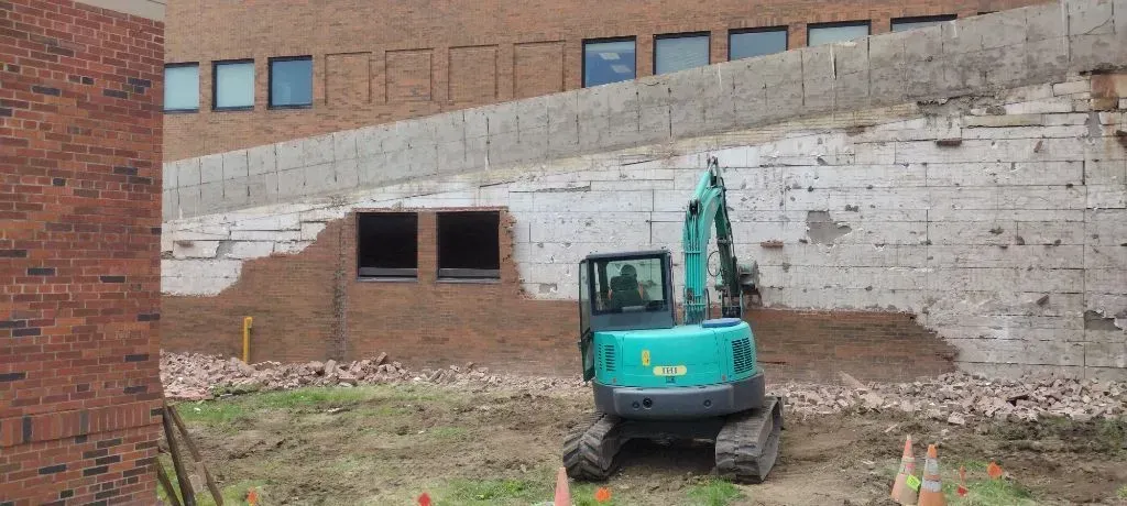 An excavator demolishes a brick wall next to a brick building. Construction zone.