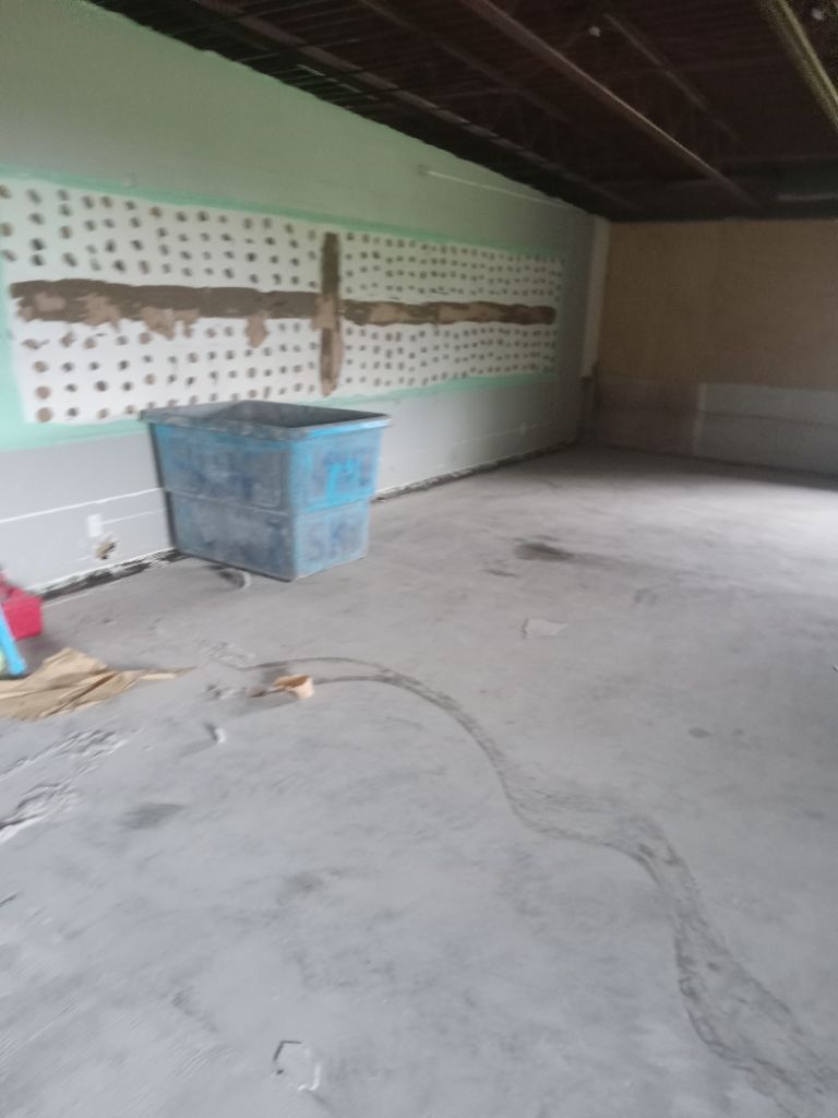 Interior of a basement with concrete floor, blue container, and wall with exposed studs.