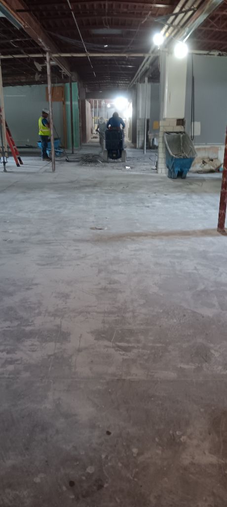 Construction site with a worker, exposed ceiling, and concrete floor.