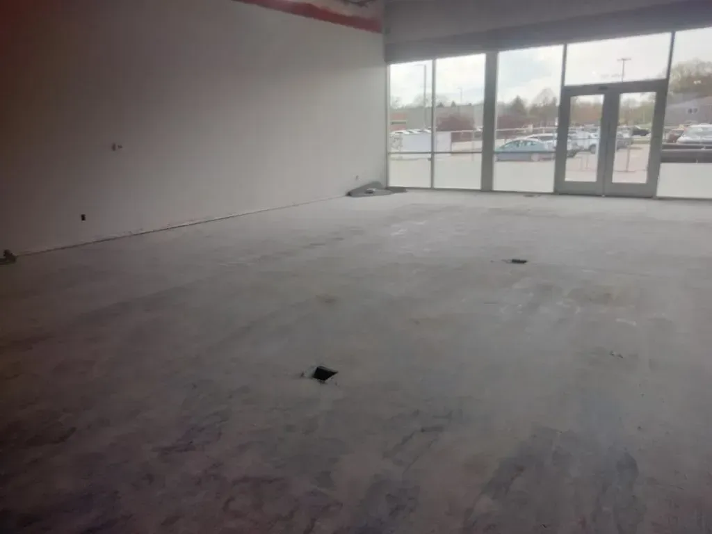 Empty, unfinished commercial space with concrete floor, large windows, and a doorway to the outside.