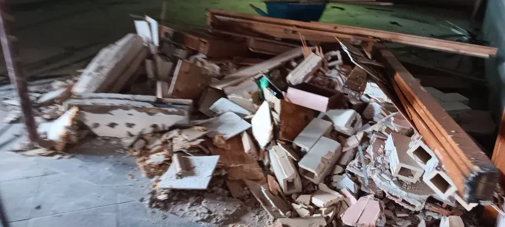 Debris pile of broken wood and tiles on a concrete floor, possibly construction or demolition.