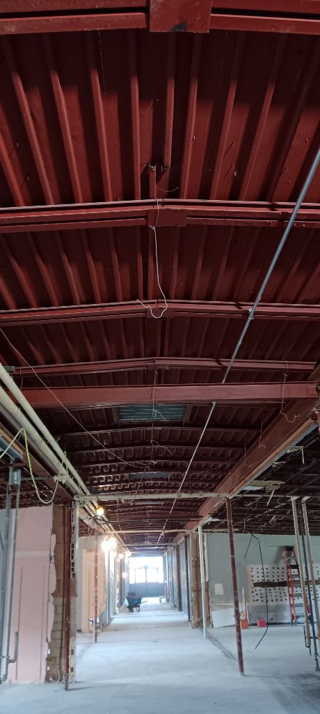 Construction site hallway with exposed ceiling beams, conduit, and unfinished walls.