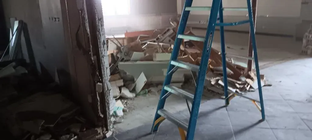 Room undergoing renovation with debris and a blue ladder.