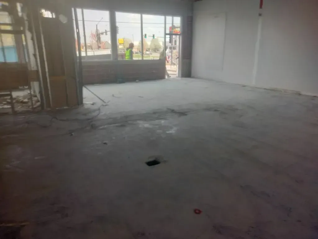 An unfinished interior space with a concrete floor and construction workers visible in the background.