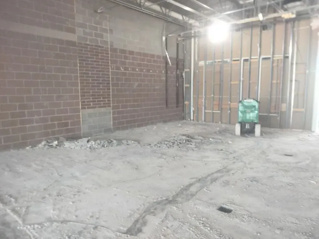 Construction site interior with brick and metal framing, debris on floor, and a green machine.