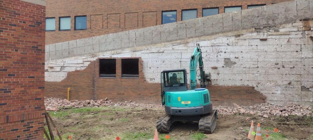 An excavator demolishing a brick building; construction site.