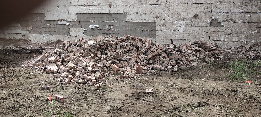Pile of broken bricks in front of a brick wall, on muddy ground. 