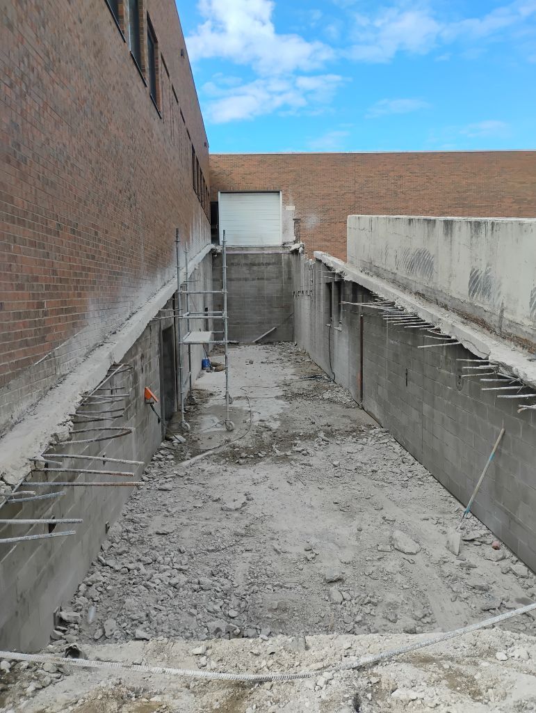 Construction site; trench dug next to a brick building, concrete debris and exposed rebar.