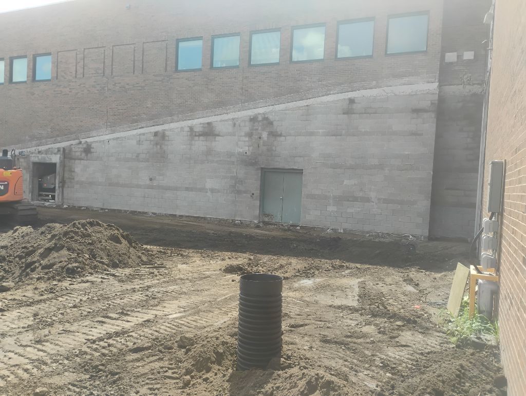 Construction site: building with windows, dirt, and a small excavator.