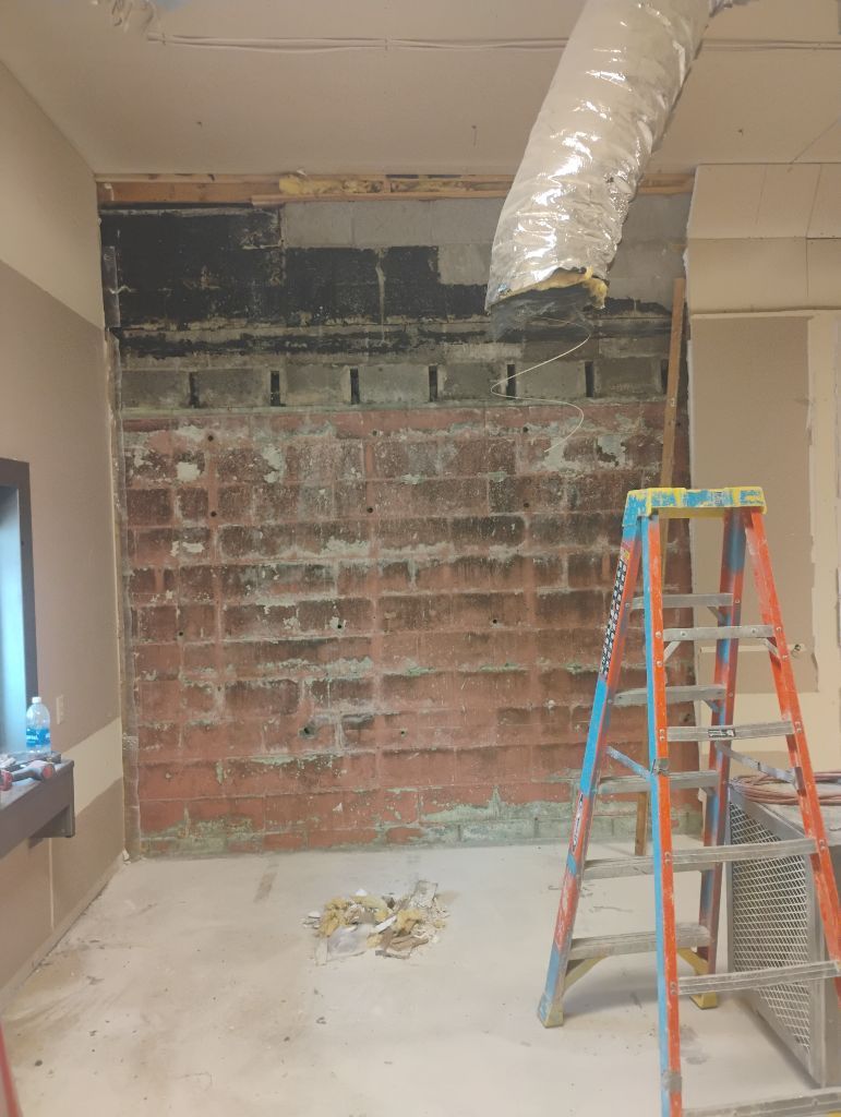 Brick wall in renovation, with ladder, exposed ductwork, and debris on the floor.