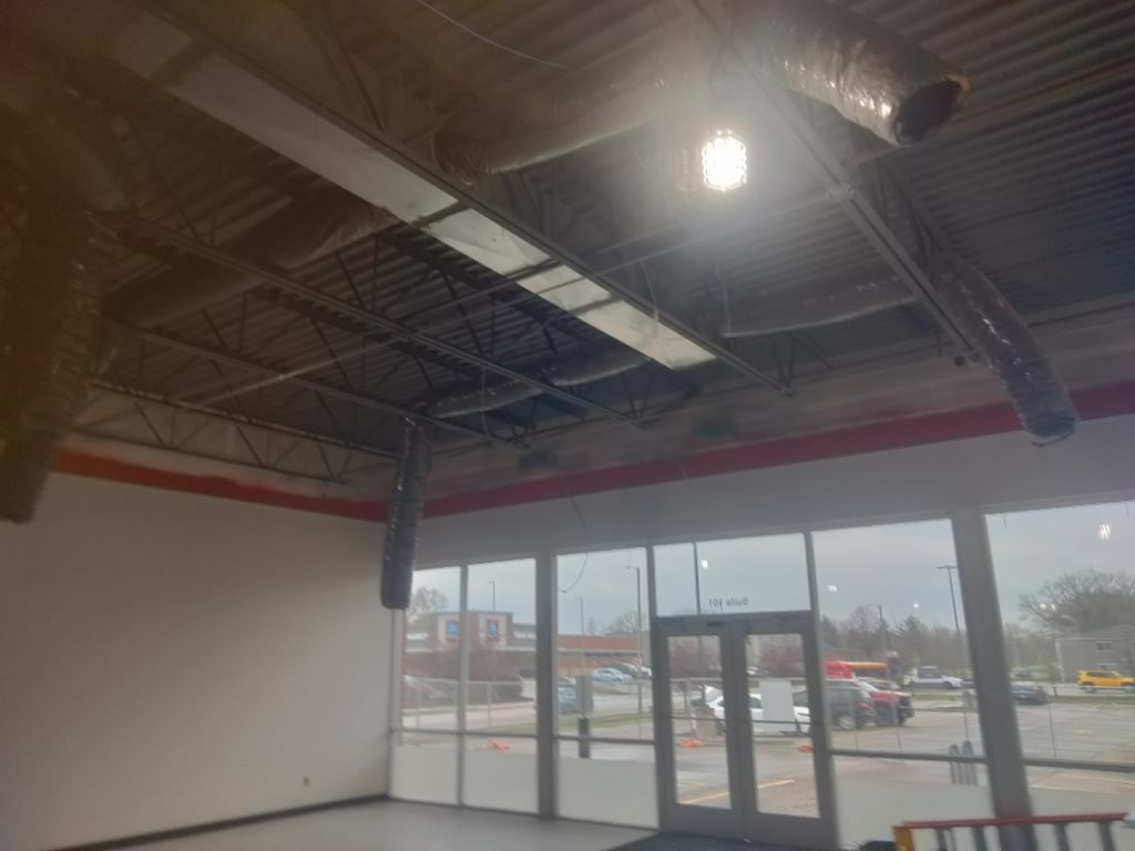Interior view of an empty commercial space with exposed ceiling and large windows looking outside.