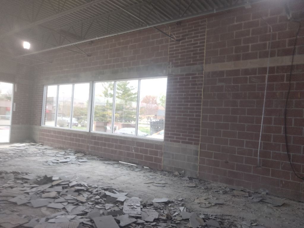 Interior of a brick-walled building under construction, windows, and debris on the floor.