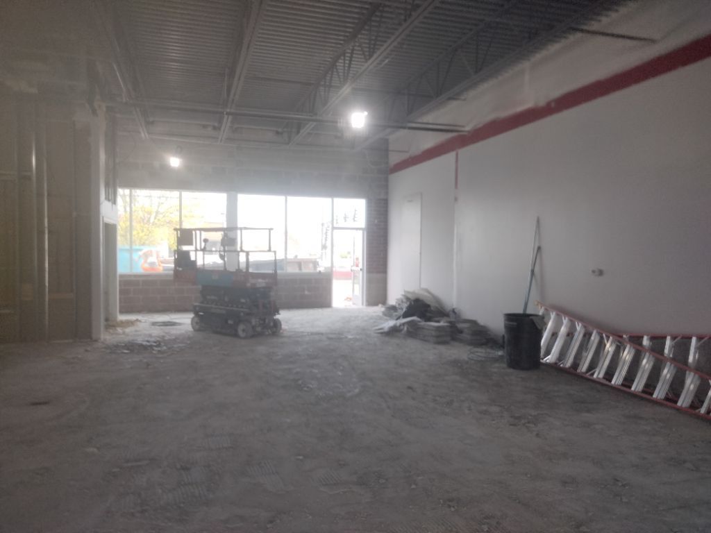 Interior of a commercial space under construction; concrete floor, white walls, front windows visible.