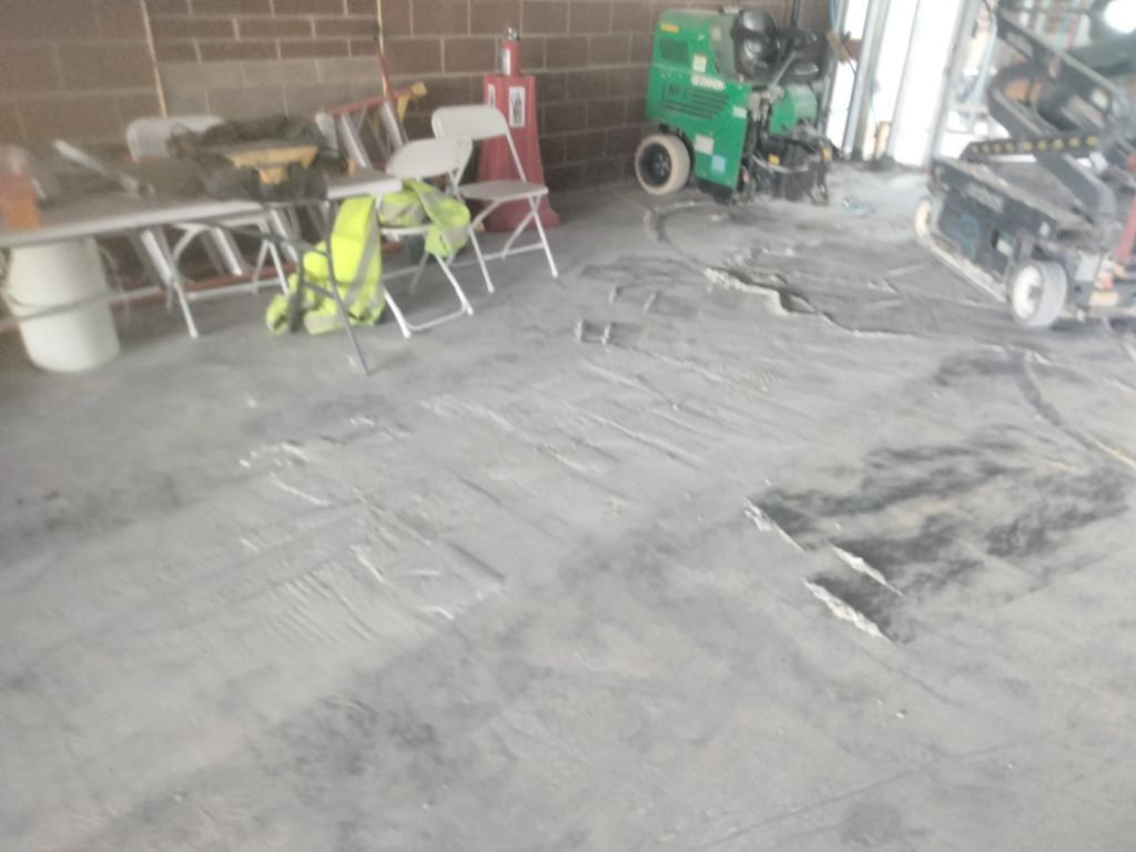 Garage interior: cracked concrete floor, tools, equipment, white table, folding chairs.