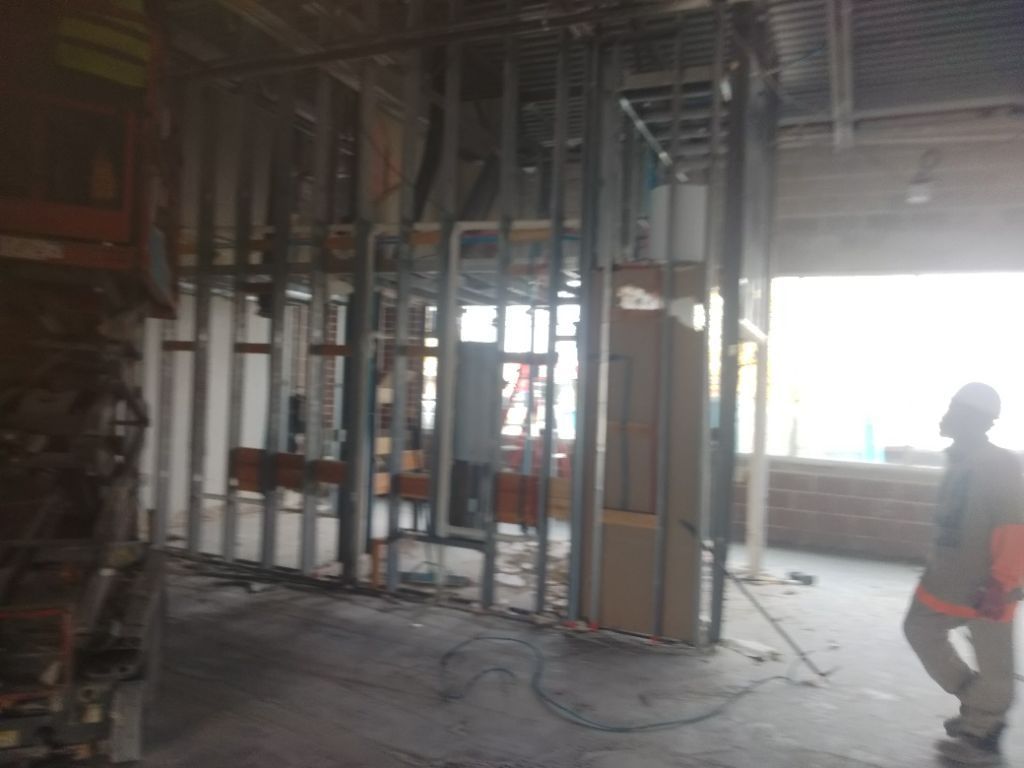 Construction site: Metal framing for walls, worker in safety vest, exposed electrical and plumbing.