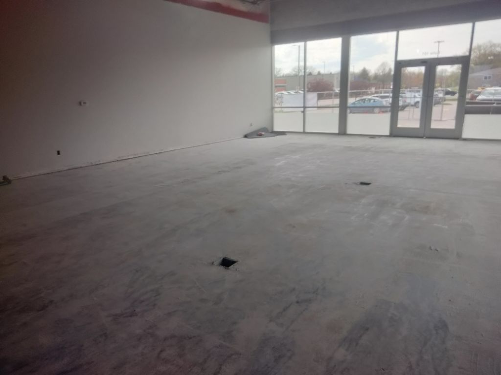 Empty commercial space with concrete floor, large windows, and unfinished walls.