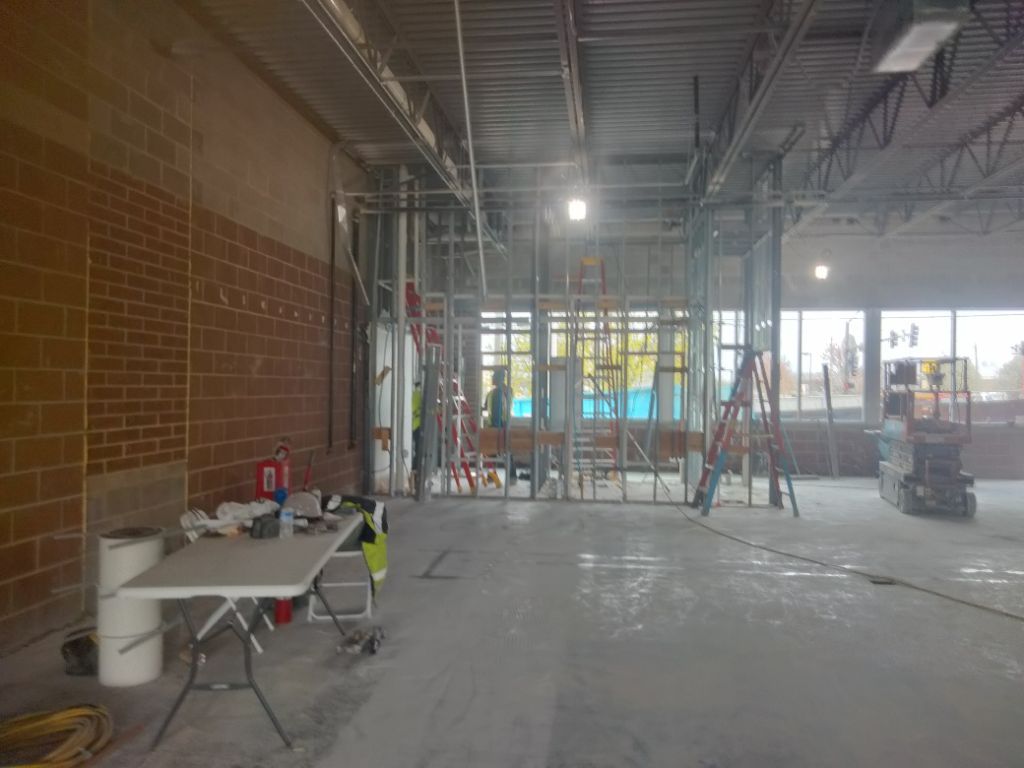 Interior construction site with exposed brick wall and metal framing; workers, ladders, and equipment visible.