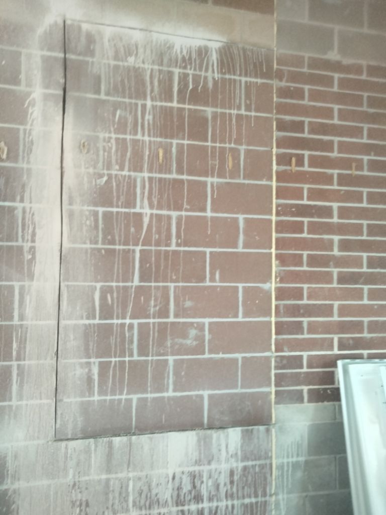 Brick wall with a sealed-off section covered in white streaks, and an adjacent wall.